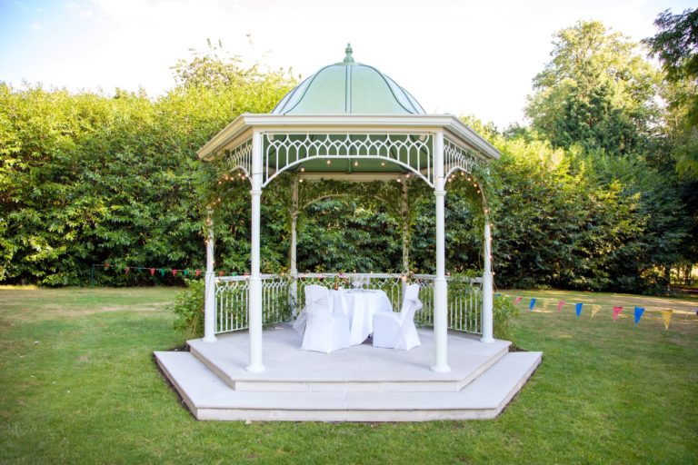 Pretty pergola on grass with bushes in the background