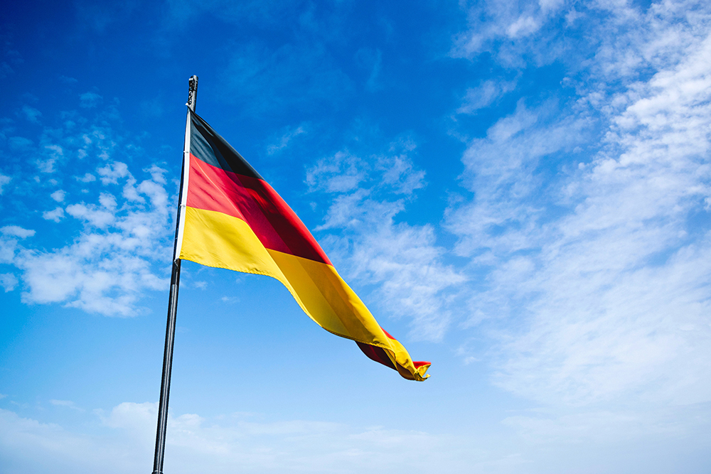 the german flag, black, red and yellow against a blue cloudy sky