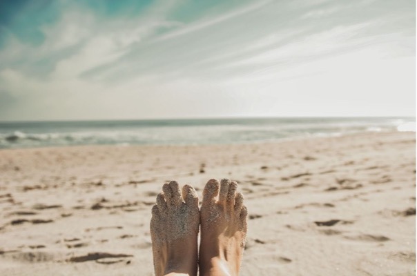 someone's sandy toes with the beach and sea and cloudy sky in the backgound