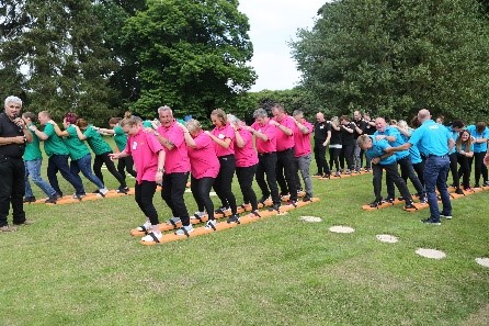 giant ski team-building event, four teams wearing pink, blue, green and black t-shirts, seven people on each of the four pairs of giant skis