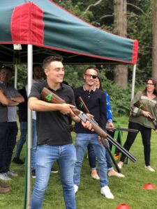 people holding clay pigeon shooting rifles. one man with eyes closed and one with black patch on one side of his classes at an outside event